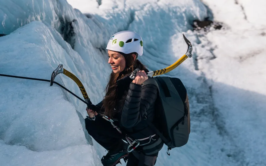 A climber with ice axes on a blue ice wall in Skaftafell, Iceland